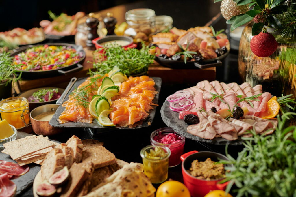 Et buffébord med diverse brød, kjøttskiver, røkelaks med lime, salater, sylteagurk, garnityr og en vase med julepynt skaper en sentral scene som minner om Ringes Ronny-feiringer.