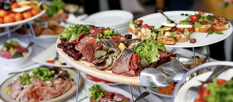 Et utvalg forretter på et cateringfat, med fokus på kjøtt og salat, ved et buffébord.