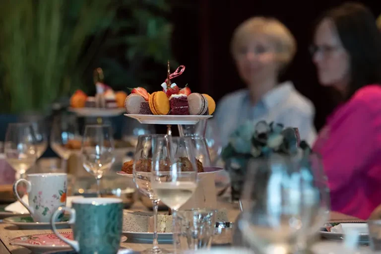 Et bord dekket med desserter, vinglass og kaffekopper; to personer står i bakgrunnen, litt ute av fokus på Hotel Centrals eksklusive smaking av sommerens bobler-arrangement.