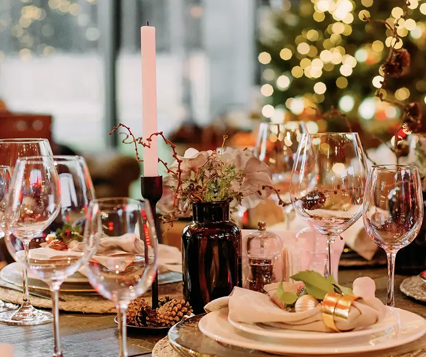 Elegant spisebord satt med glass, et stearinlys, og festlig innredning som minner om Central Restaurant og Bar, med et uskarpt juletre i bakgrunnen.