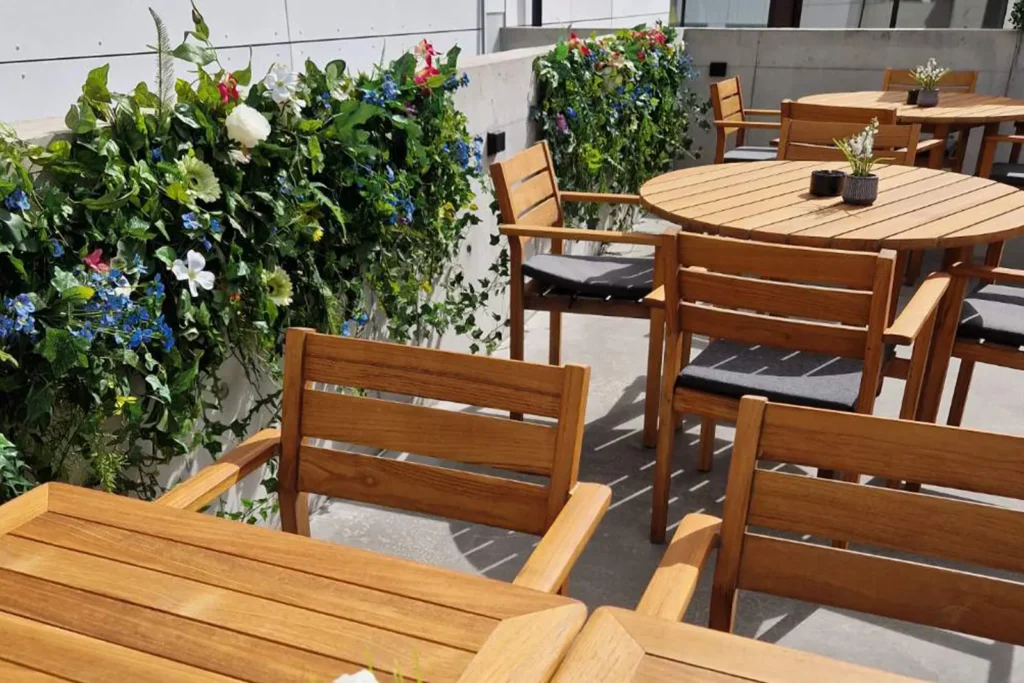 Uteplass med runde og firkantede trebord og stoler; en betongvegg dekorert med grønne planter og fargerike blomster – perfekt for å feire 17. mai på Central Restaurant & Bar.