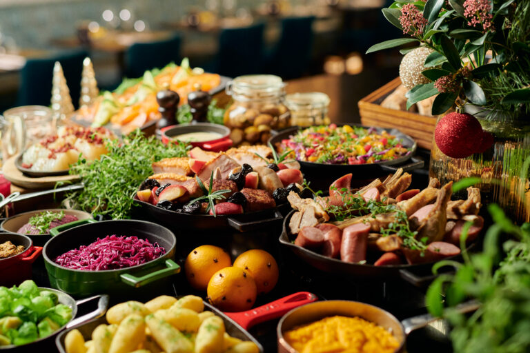 Et buffébord med ulike retter som pølser, grønnsaker, salat, poteter, frukt og garnityr er dekket til en festlig smaking av sommerens bobler på Hotel Central. Festlige dekorasjoner skaper en livlig bakgrunn.